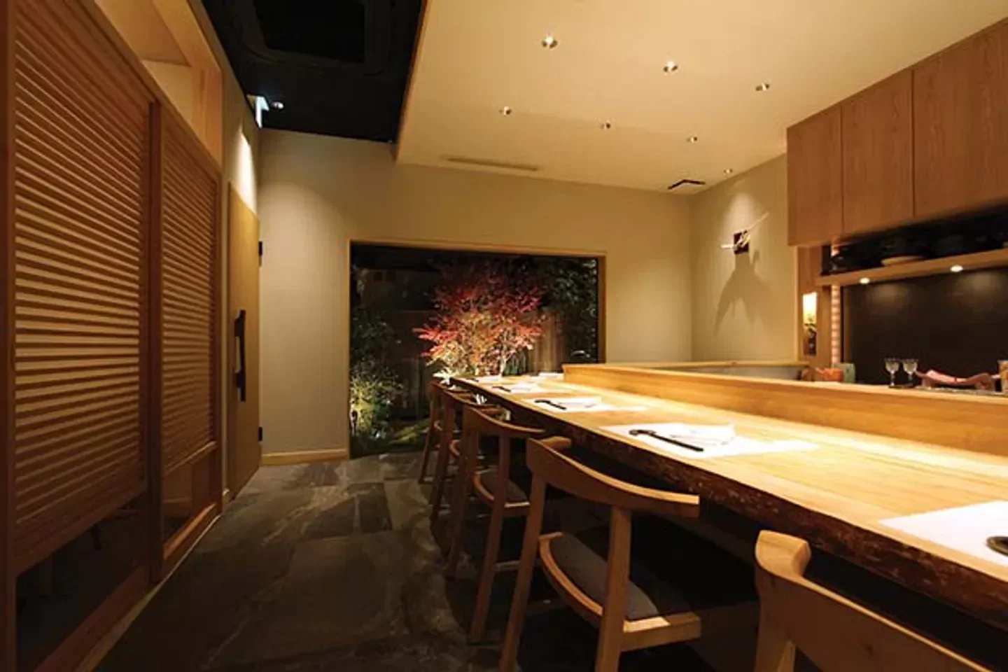 Interior dining at Shirosaka in Tokyo. Features a wooden counter and a view of a garden.