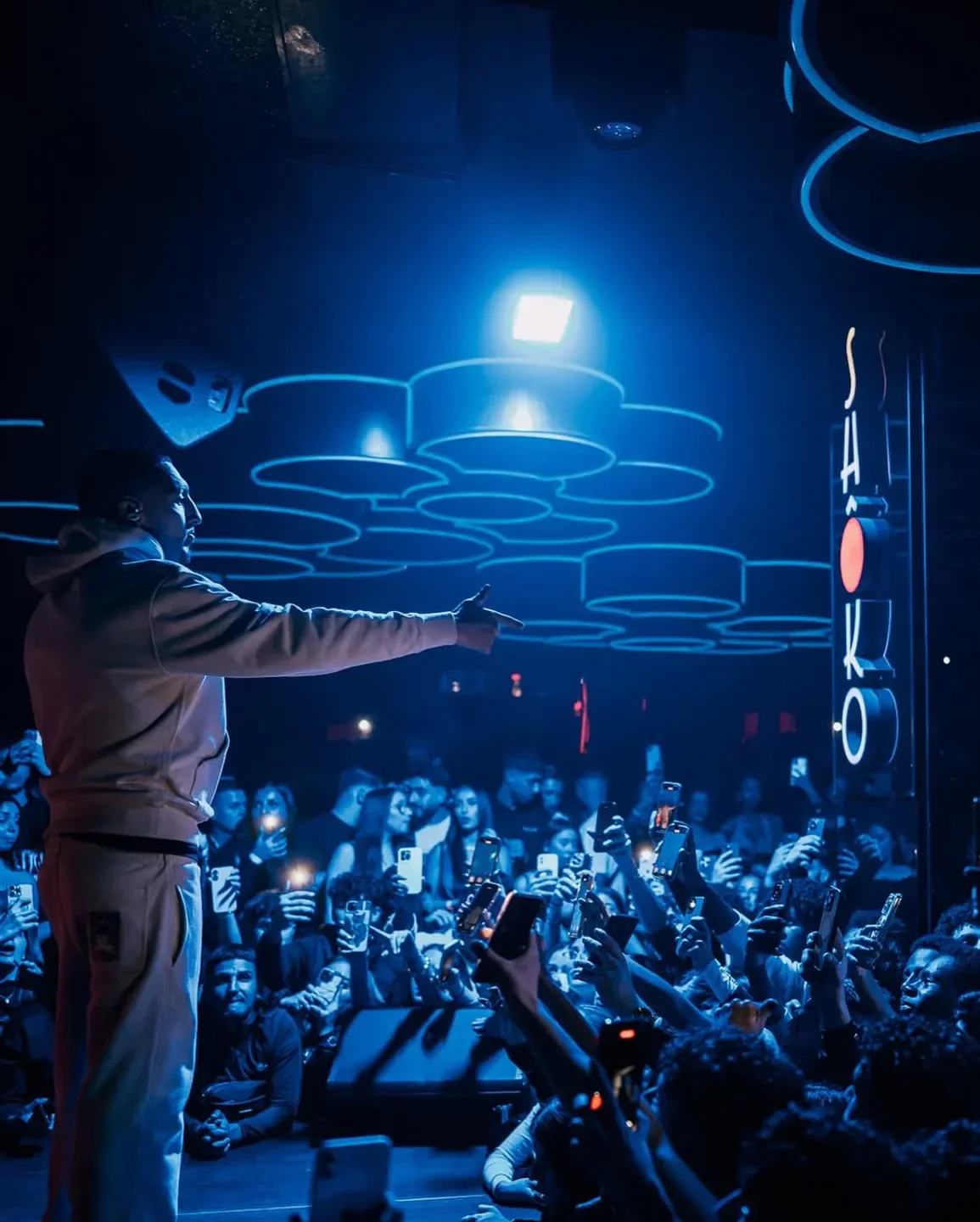 Energetic crowd at Shoko Barcelona nightclub, with artist performing under stage lights.