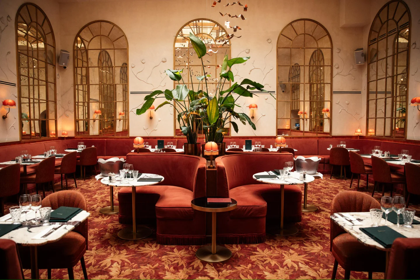 Siena restaurant interior in Paris featuring plush red banquettes, elegant arched mirrors, and ornate carpeting.