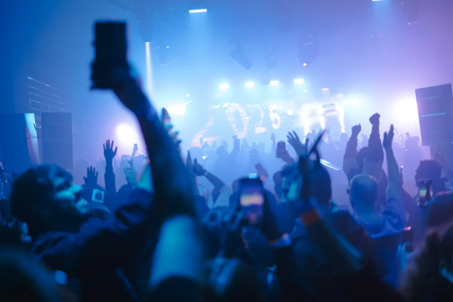 Crowd with hands in the air at Sky Club Malta enjoying a concert with bright stage lights.