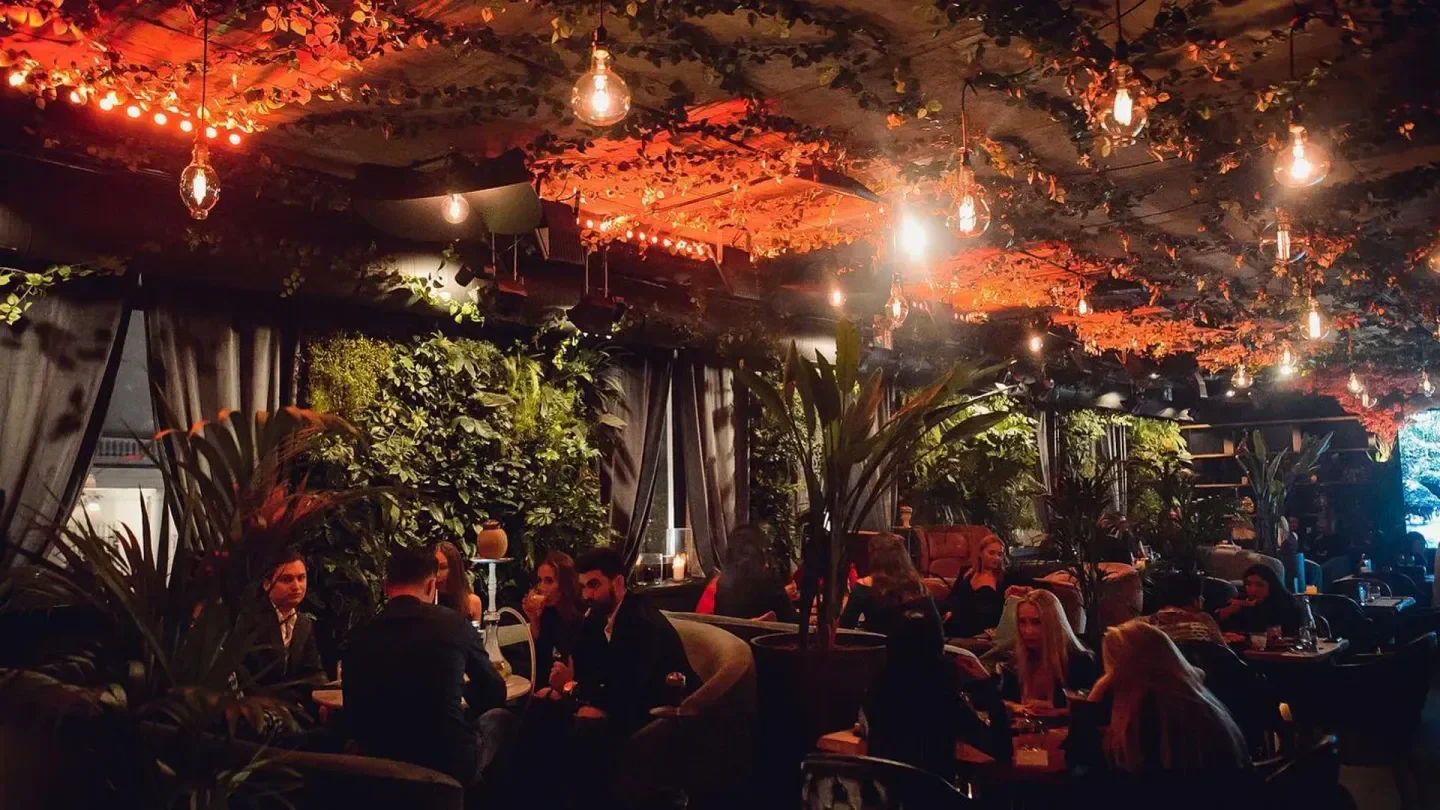 Interior of SLA nightclub in Warsaw, with lush plants, ambient lighting, and patrons.