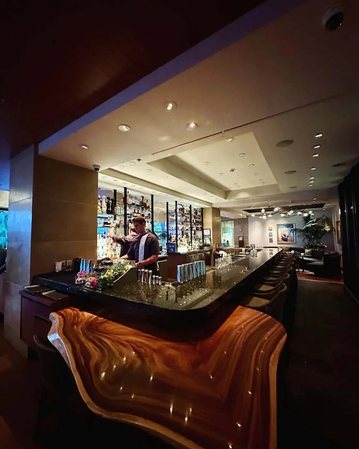 Interior bar at Spago in Maui, featuring a bartender and stylish, wooden counter.