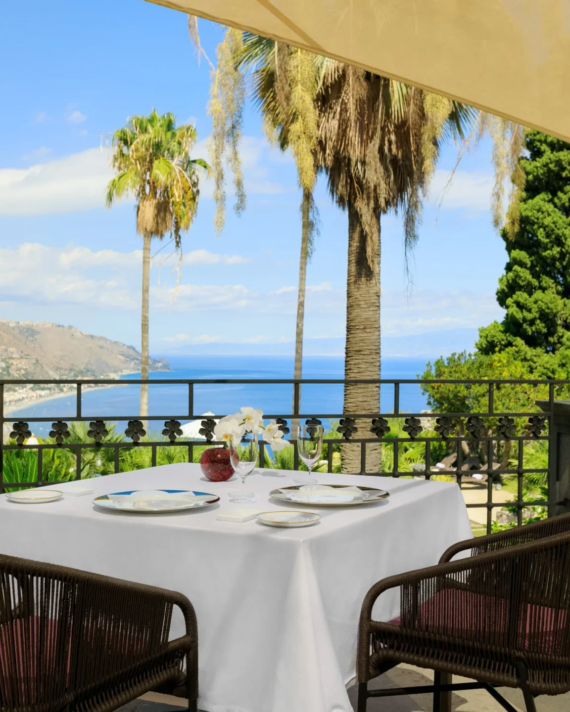 St. George Restaurant by Heinz Beck Sicily offers a table with a stunning sea view and palm trees.