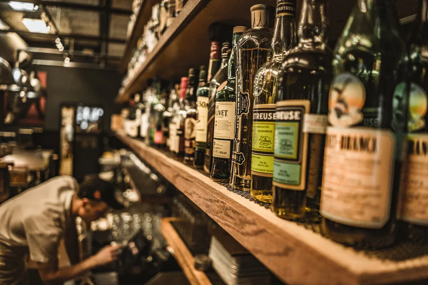 Shelves of spirits at St. Roch Fine Oysters Bar in Raleigh with staff in the background.