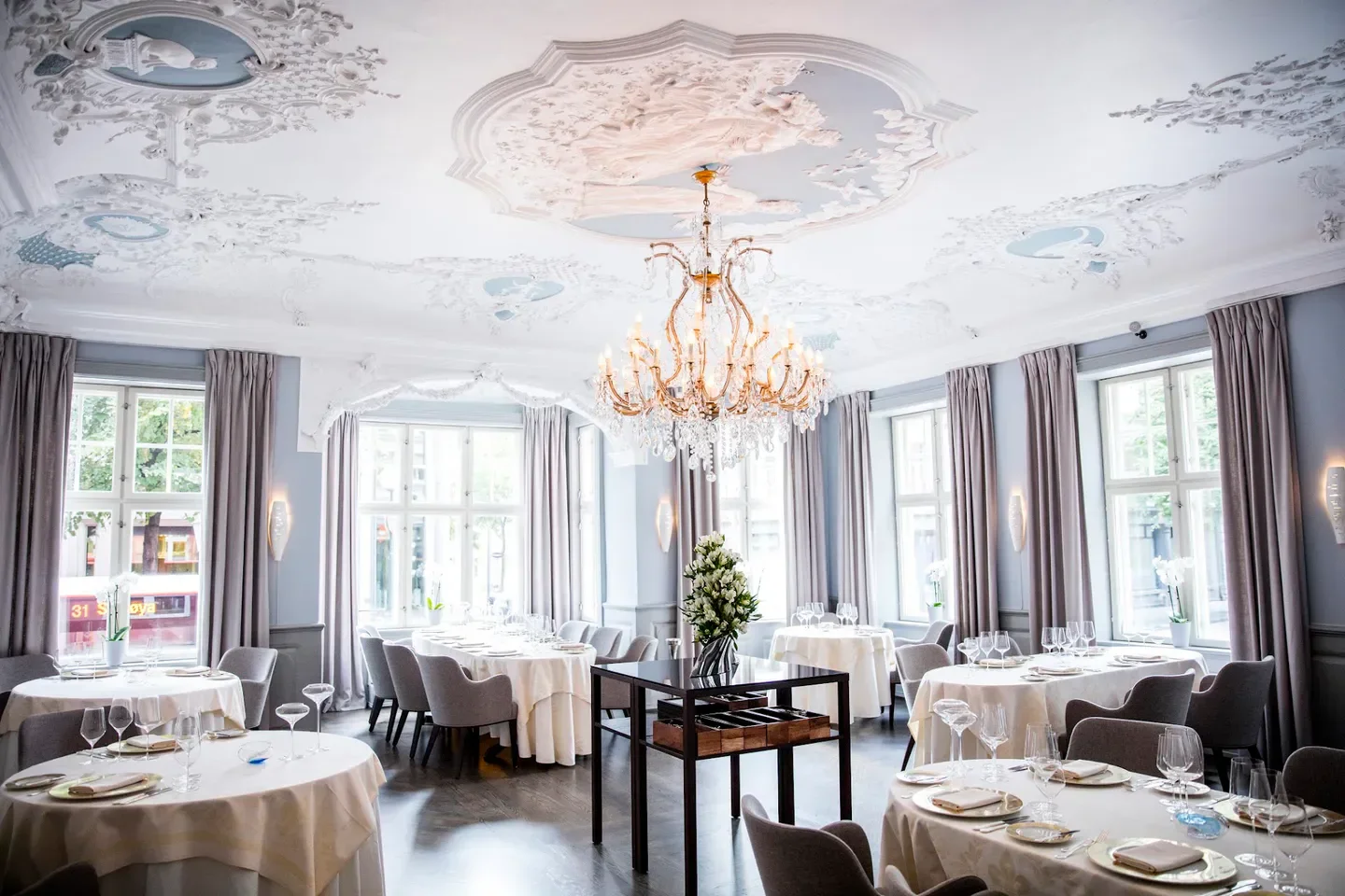 Elegant dining room at Statholdergaarden restaurant in Oslo with ornate ceiling and chandelier.