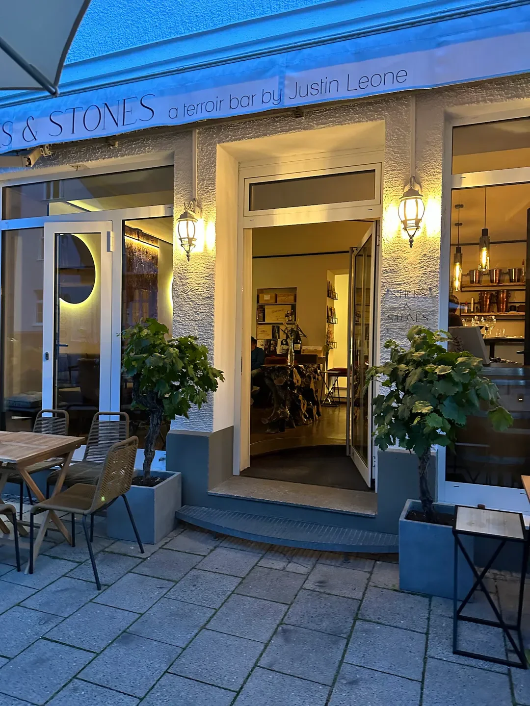 Entrance to Sticks & Stones restaurant in Munich, with outdoor seating and warm lighting.