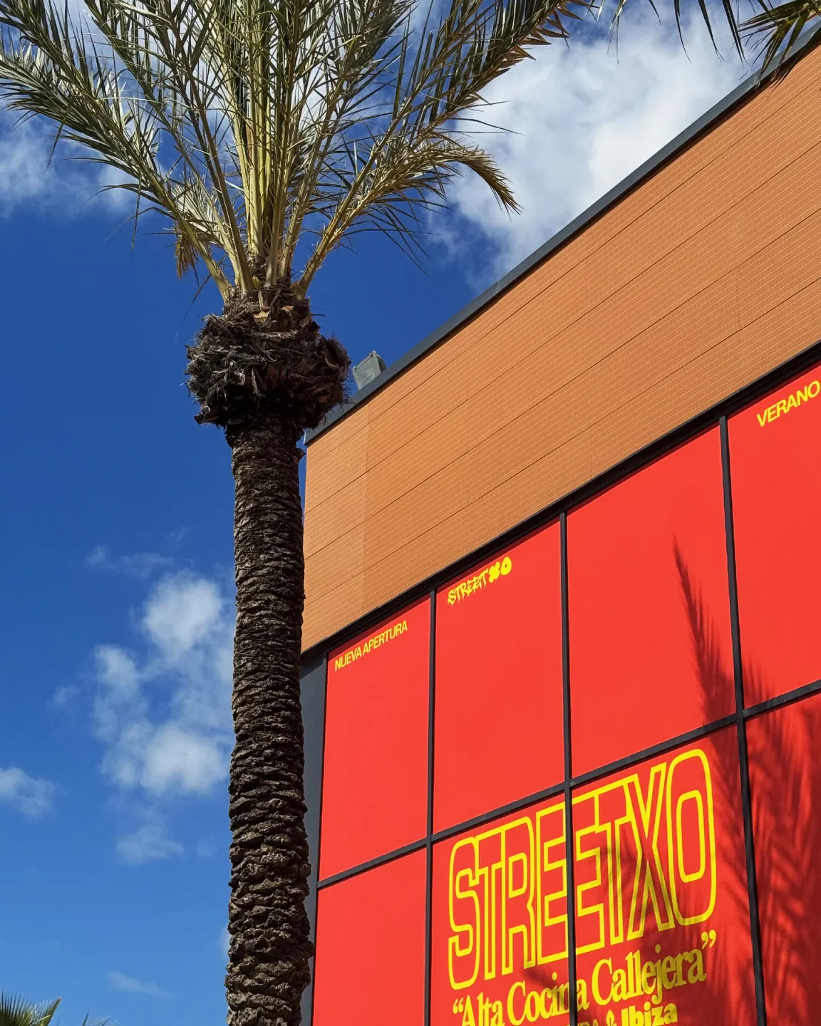 StreetXO Ibiza restaurant facade with bright red panels and a prominent palm tree against a blue sky.