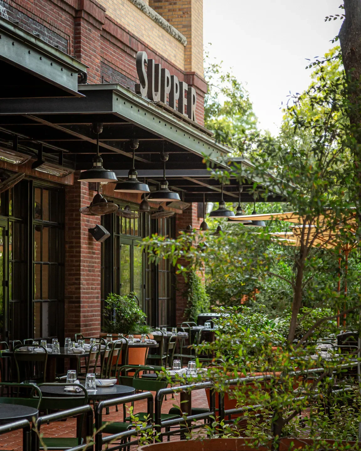 Outdoor dining at Supper American Eatery in San Antonio, Texas with lush greenery.