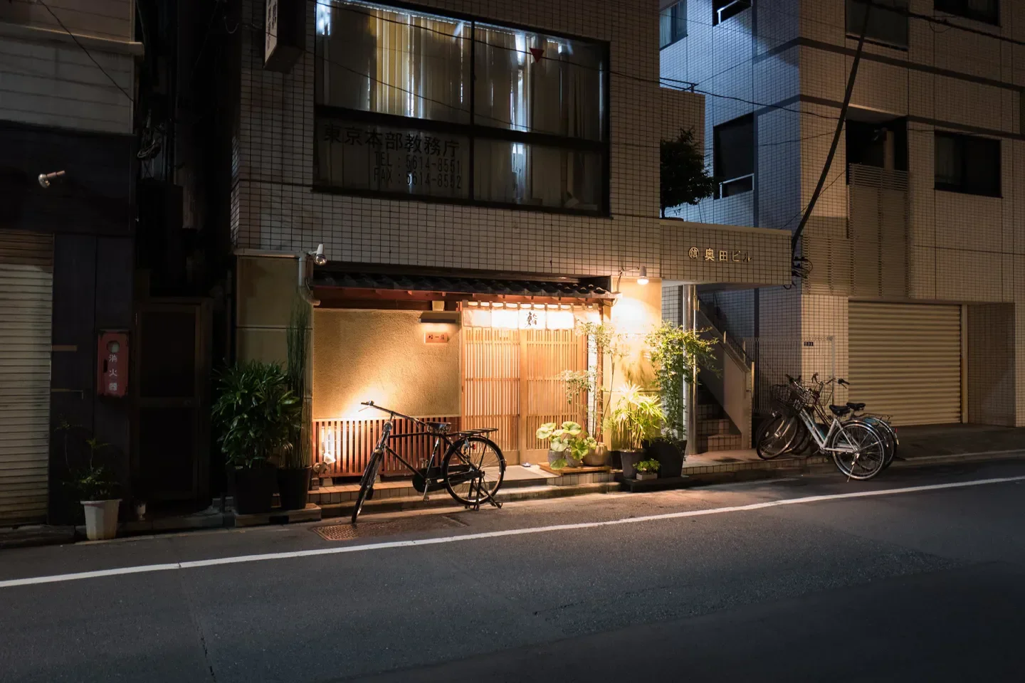 Exterior of Sushi Ichijo in Tokyo at night, featuring bicycles and illuminated entrance.