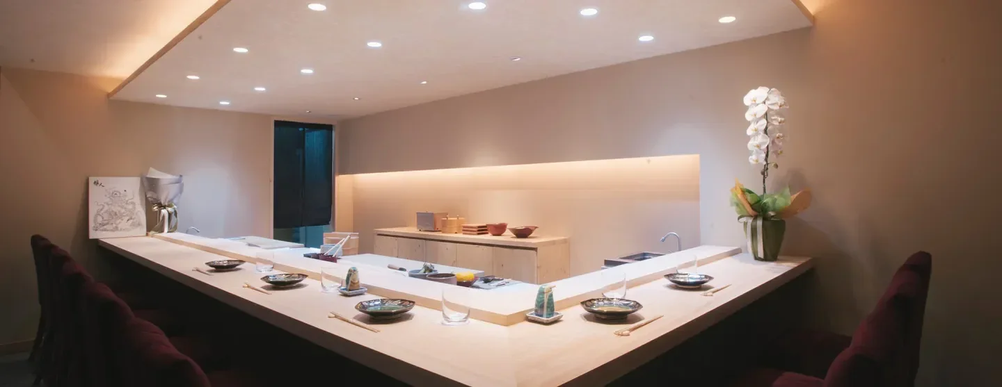 Minimalist interior of Sushi Masato restaurant in Bangkok, featuring sushi bar and orchids.