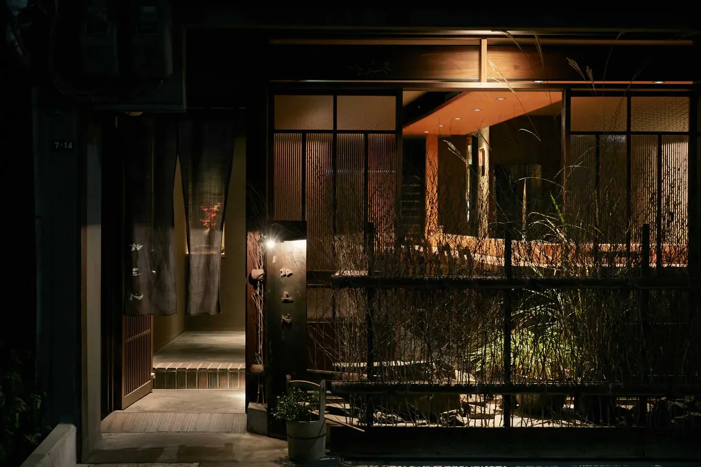 Entrance to Sushi Sanshin in Osaka, a warmly lit Japanese restaurant at night.