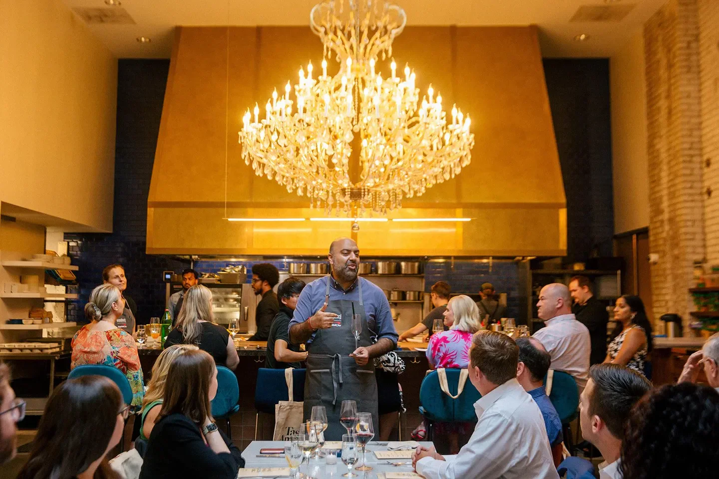 Chef speaking at TAILOR Nashville restaurant with guests in Nashville, under a chandelier.