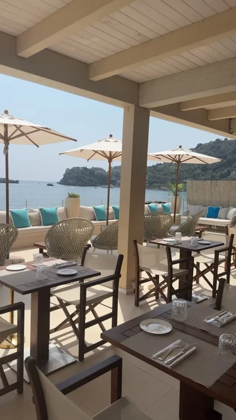 Tables set on the terrace at Tao Beach Club Taormina, Sicily, with sea views and umbrellas.