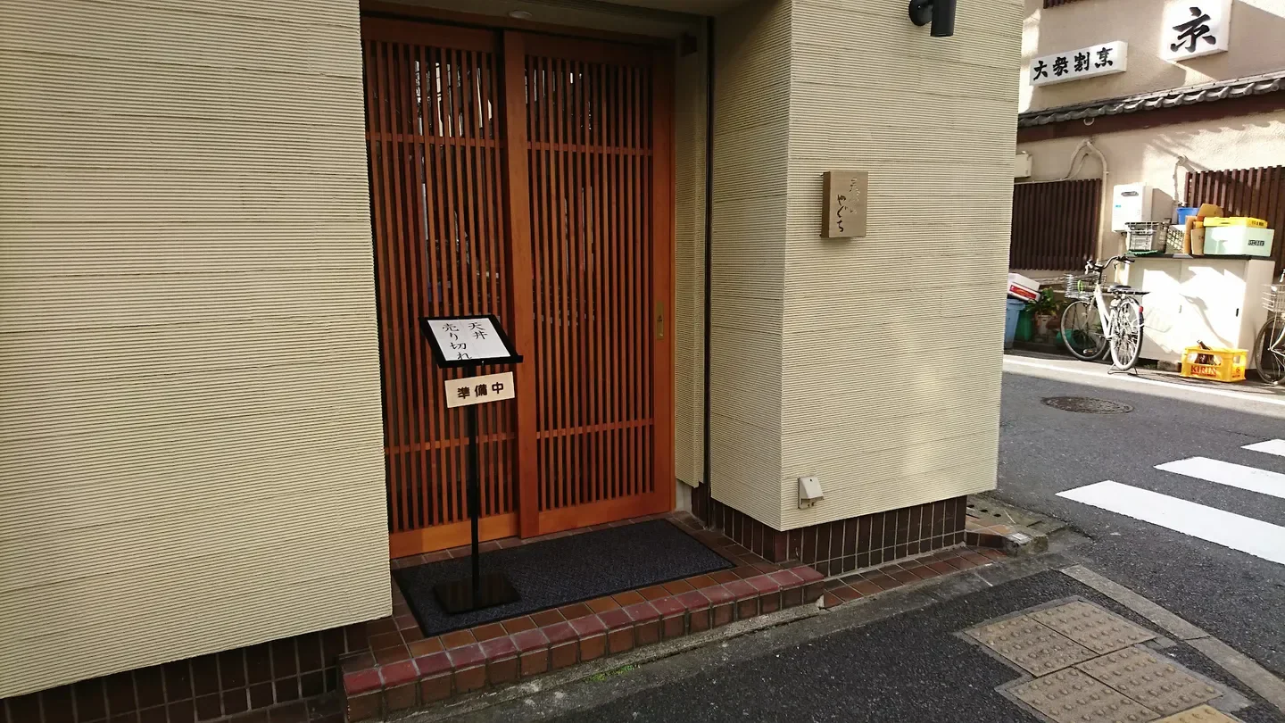 Entrance of Tempura Yaguchi in Tokyo, Japan, featuring wooden door and sign.