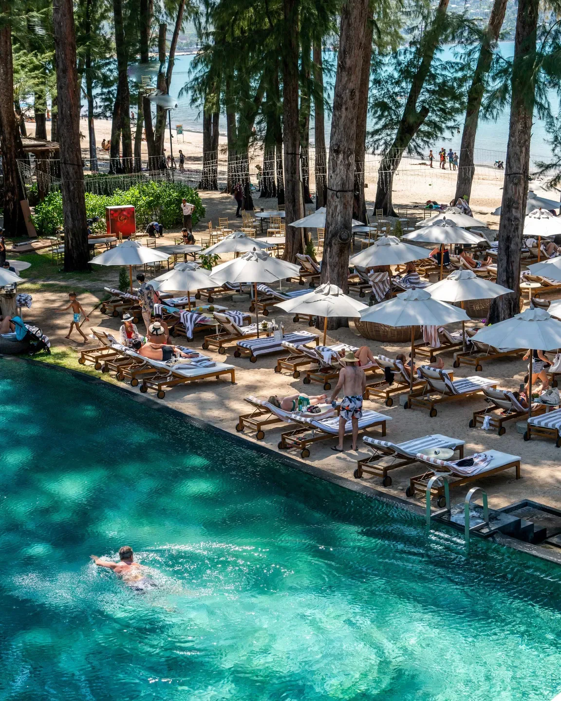 Tengoku Phuket: a serene pool scene with sunbeds and beach umbrellas by the sea.