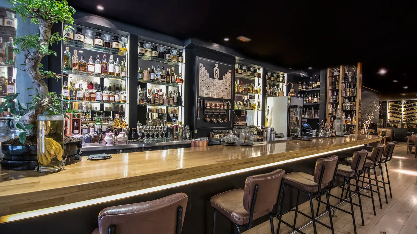 Interior of The Alchemix restaurant in Barcelona, showing bar and liquor display.