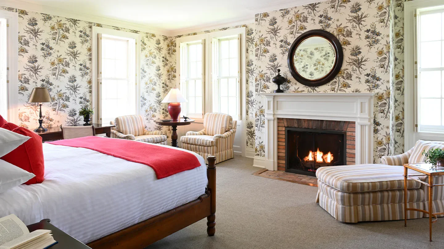 Cozy bedroom at The Aurora Inn in Saratoga, featuring a fireplace and floral wallpaper.