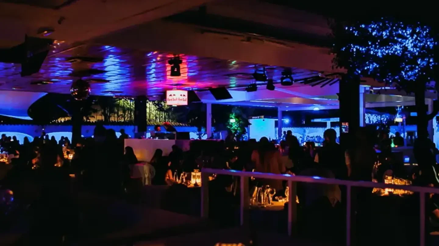 Night view of The Beach Club in Milan, with patrons and vibrant lighting.