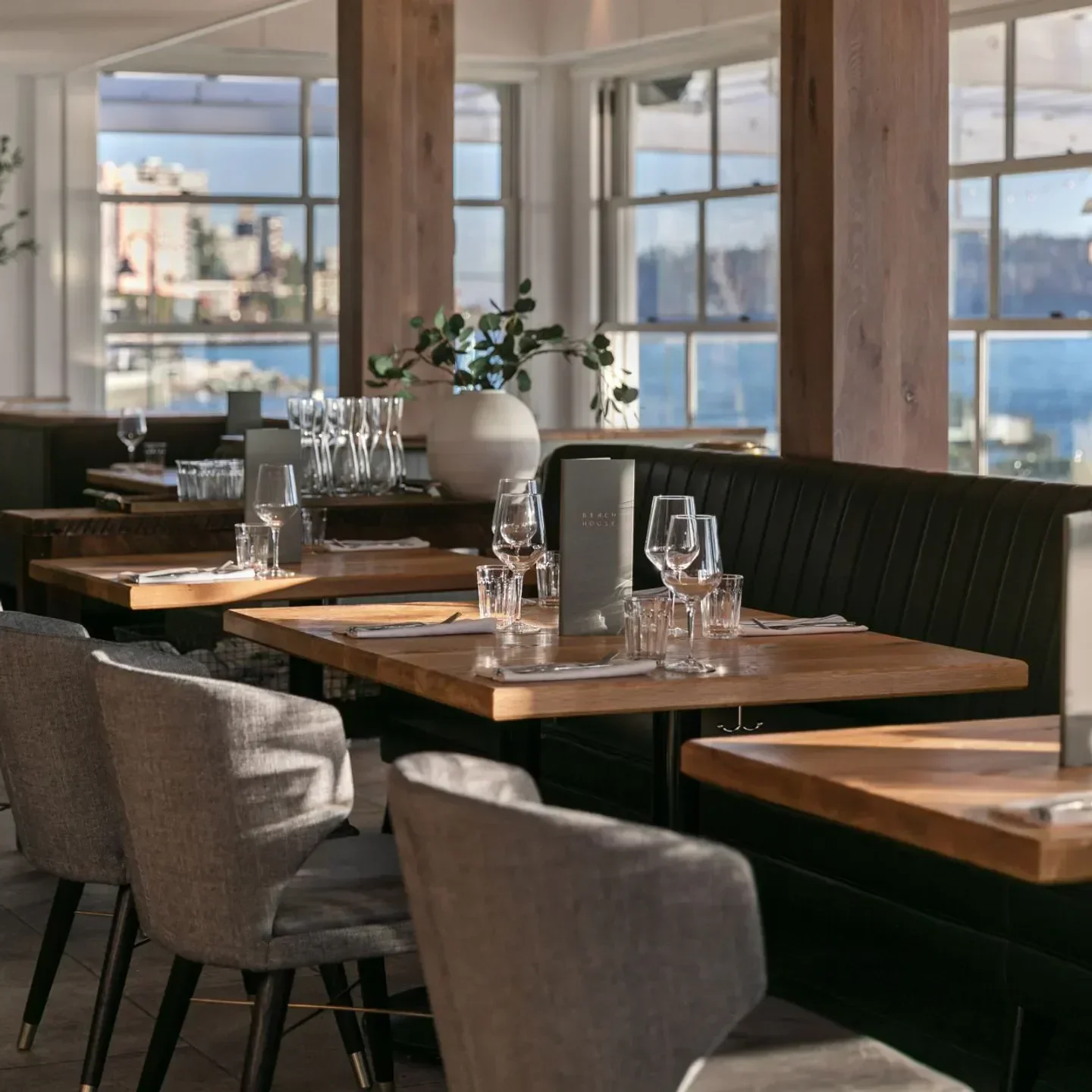 Interior of The Beach House Restaurant in Vancouver, with tables set and city view.