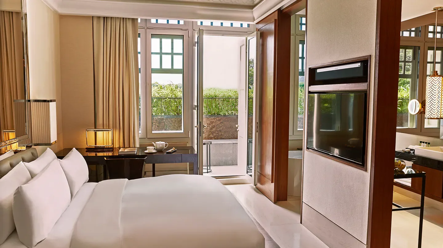 Spacious bedroom at The Capitol Kempinski Hotel Singapore with balcony and city view.