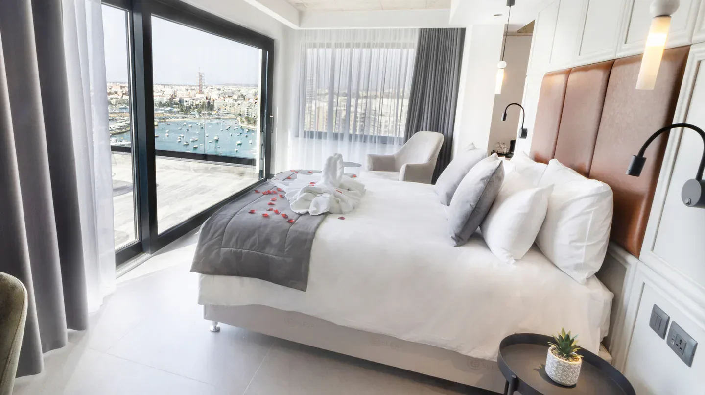 Cozy bedroom at The Londoner Hotel Sliema, Malta, with balcony view of the city.