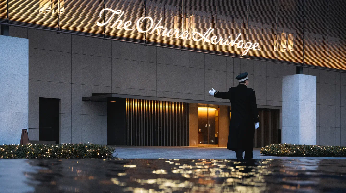 Doorman at The Okura Heritage Tokyo hotel entrance in Tokyo, reflecting pool.