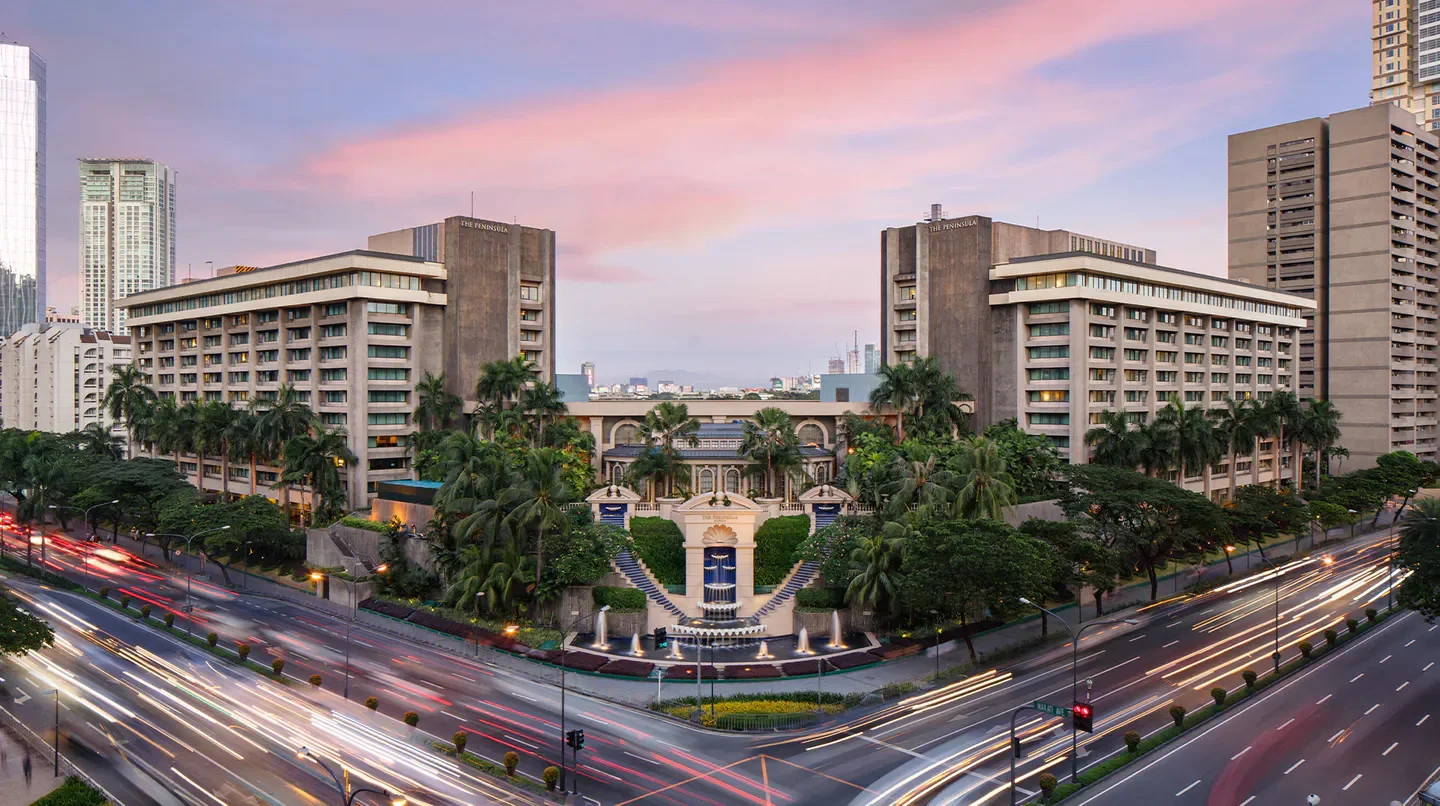 The Peninsula Manila hotel in Manila at dusk with traffic light trails and fountain.