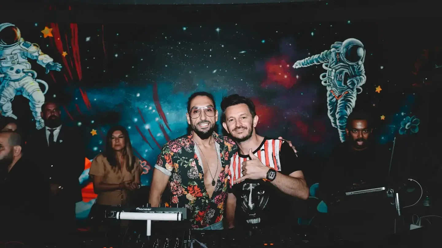 Two men at The Penthouse Zurich posing in front of a space-themed mural.