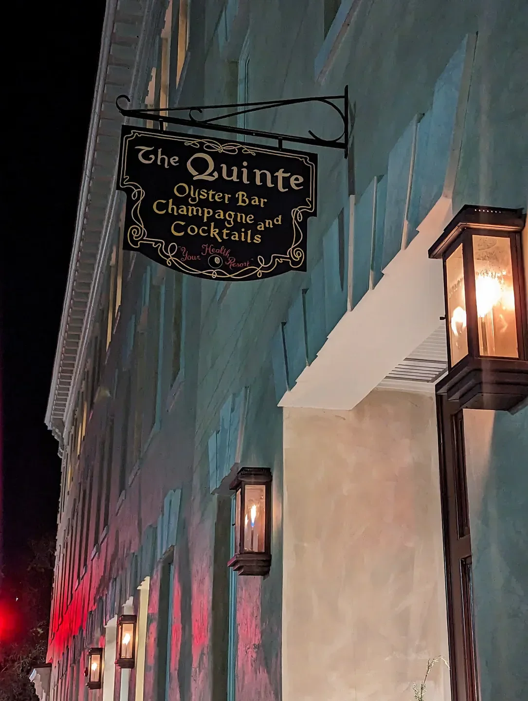 Sign for The Quinte Oyster Bar in Charleston, lit at night with wall sconces.