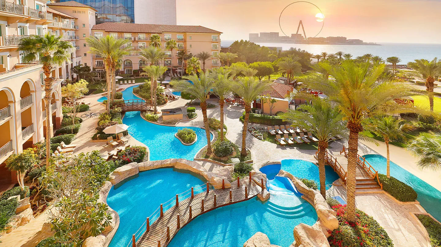 Aerial view of The Ritz-Carlton, Dubai pools and palm trees in Dubai at sunset.