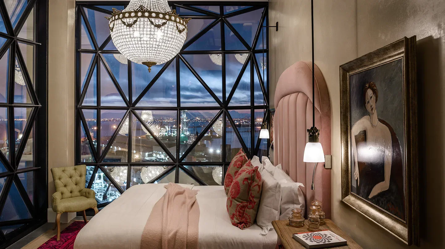 Luxury bedroom at The Silo Hotel in Cape Town with city skyline view and chandelier.