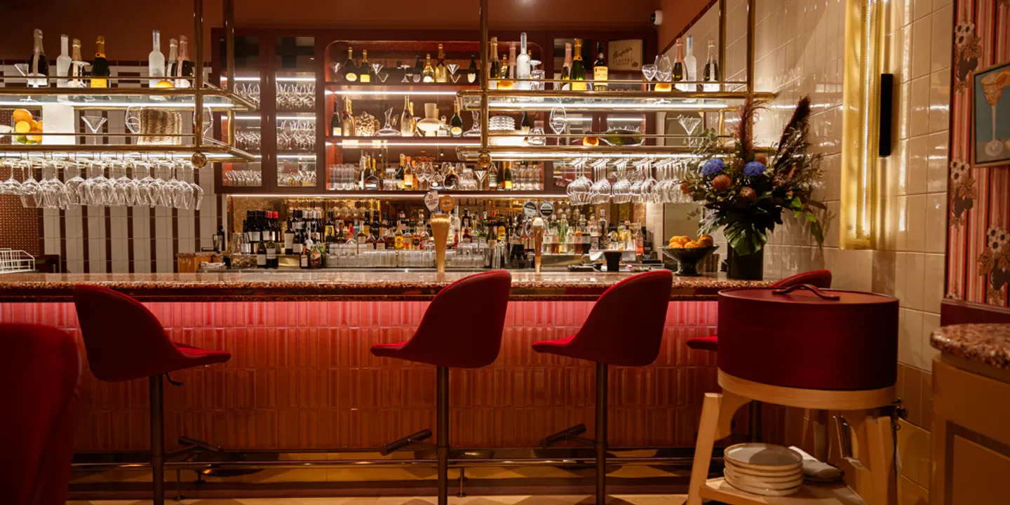 Interior of The Wolf restaurant in Brisbane, showing bar with red stools and shelves of drinks.