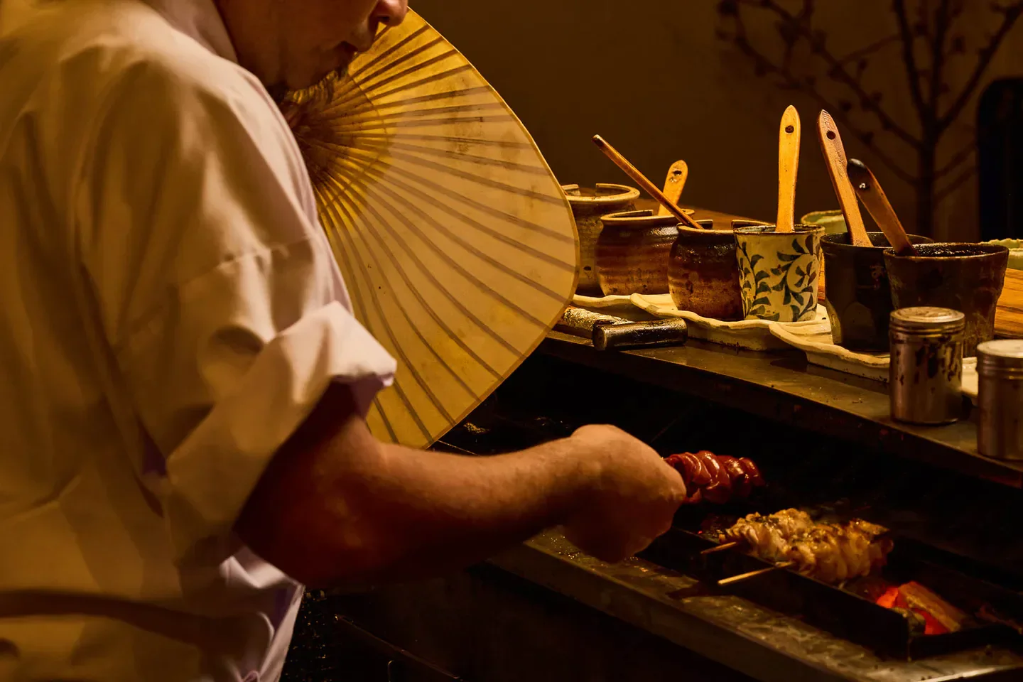 Chef grilling yakitori skewers at Torishiki restaurant in Tokyo with a traditional fan