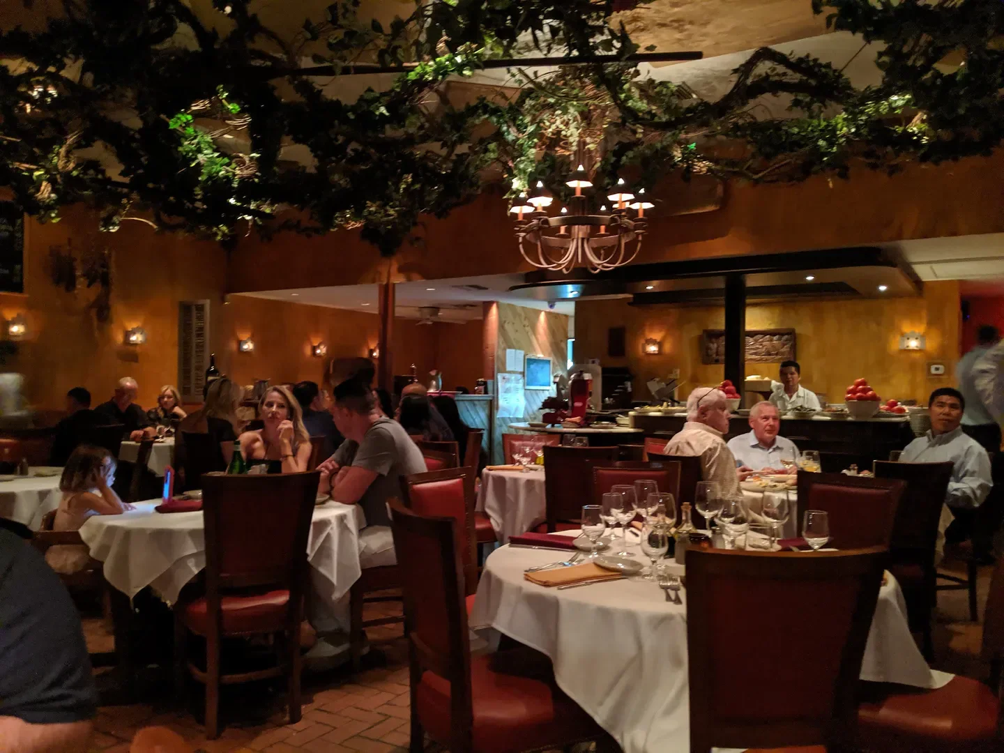 Cozy dining room at Trattoria Romana in Palm Beach, with chandeliers and tables set.