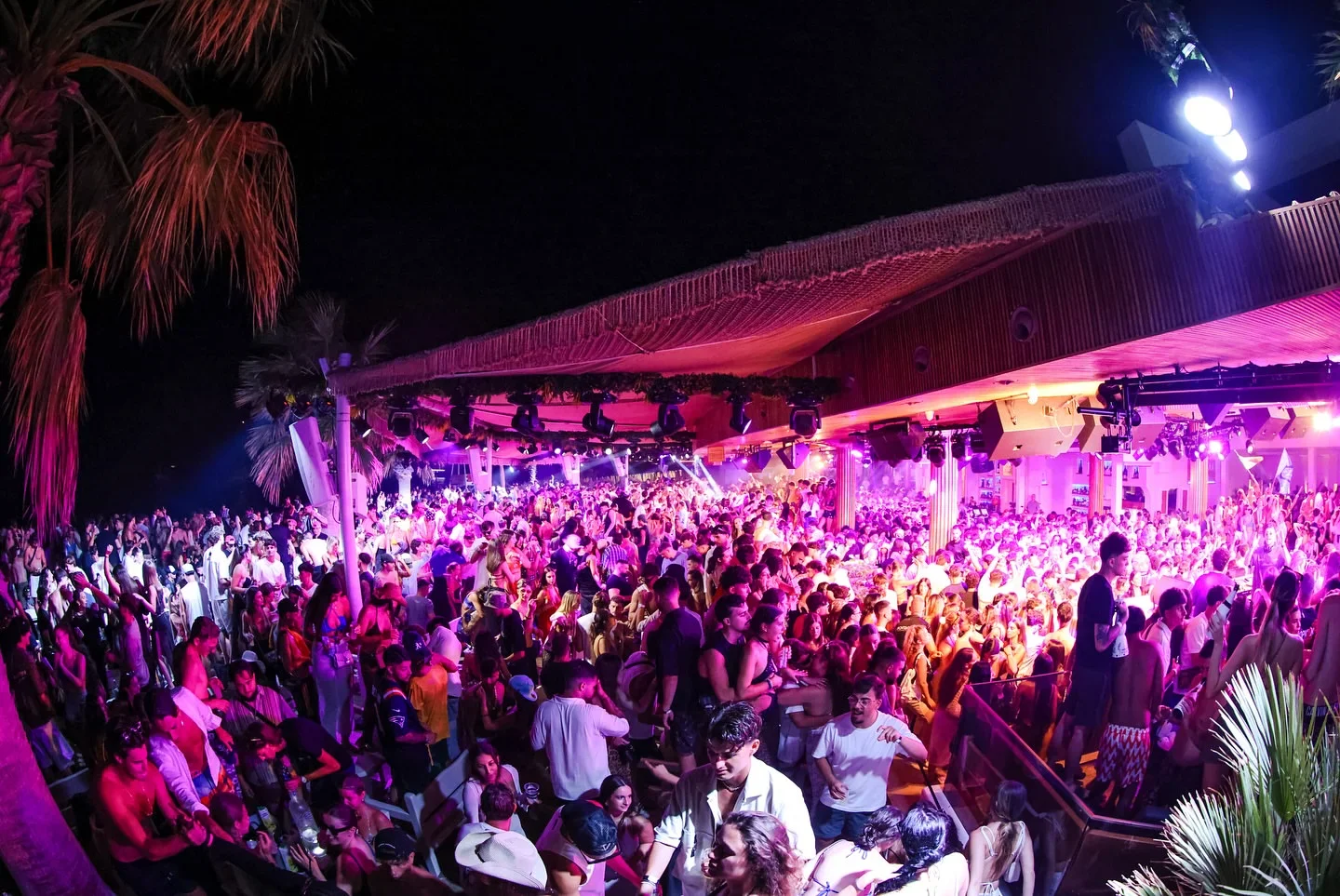 Nightlife scene at Tropicana beach club in Mykonos, Greece with a large crowd dancing under the lights.