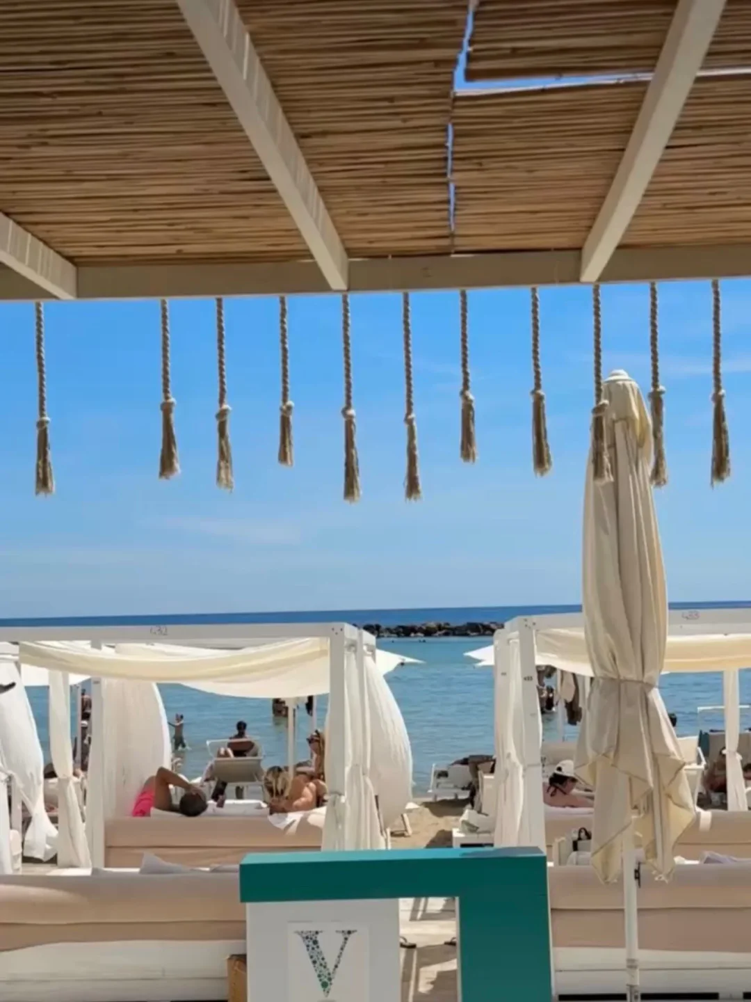 Relaxing cabanas at V Lounge Beach in the city with people enjoying the ocean view and sunny weather.