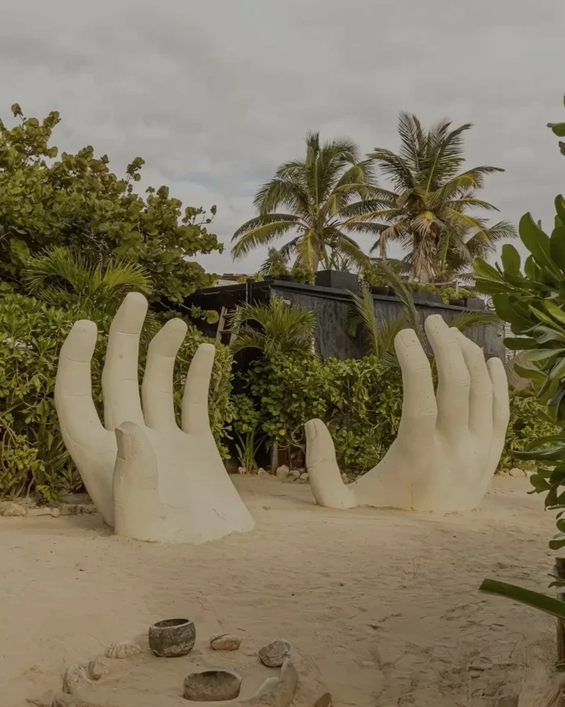 Giant hand sculpture at Vagalume beach club in Tulum, Mexico, surrounded by lush tropical greenery and sand.