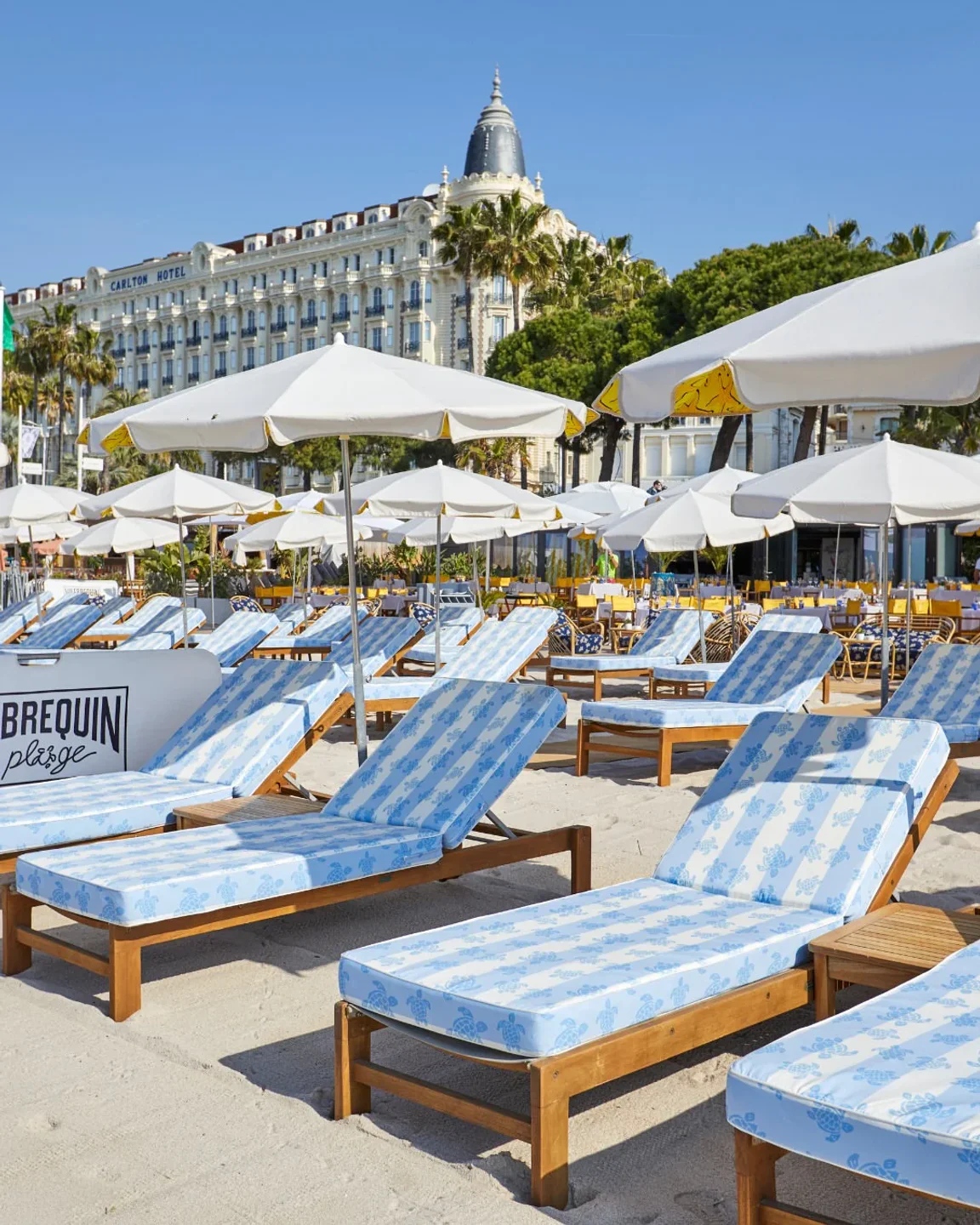 Vilebrequin La Plage restaurant in Cannes with blue striped beach chairs and umbrellas on a sunny day.