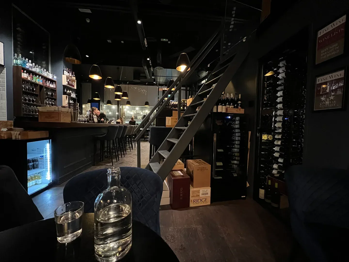 Interior of VIN Bjørvika in Oslo, showing bar, wine bottles, and staircase.