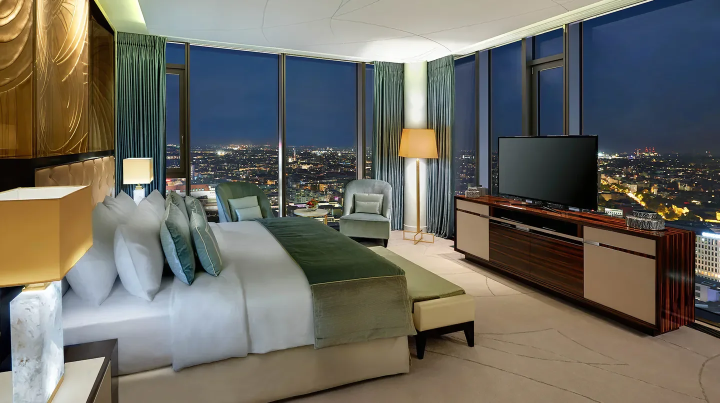 Luxury bedroom with city views at Waldorf Astoria Berlin, showcasing Berlin at night.