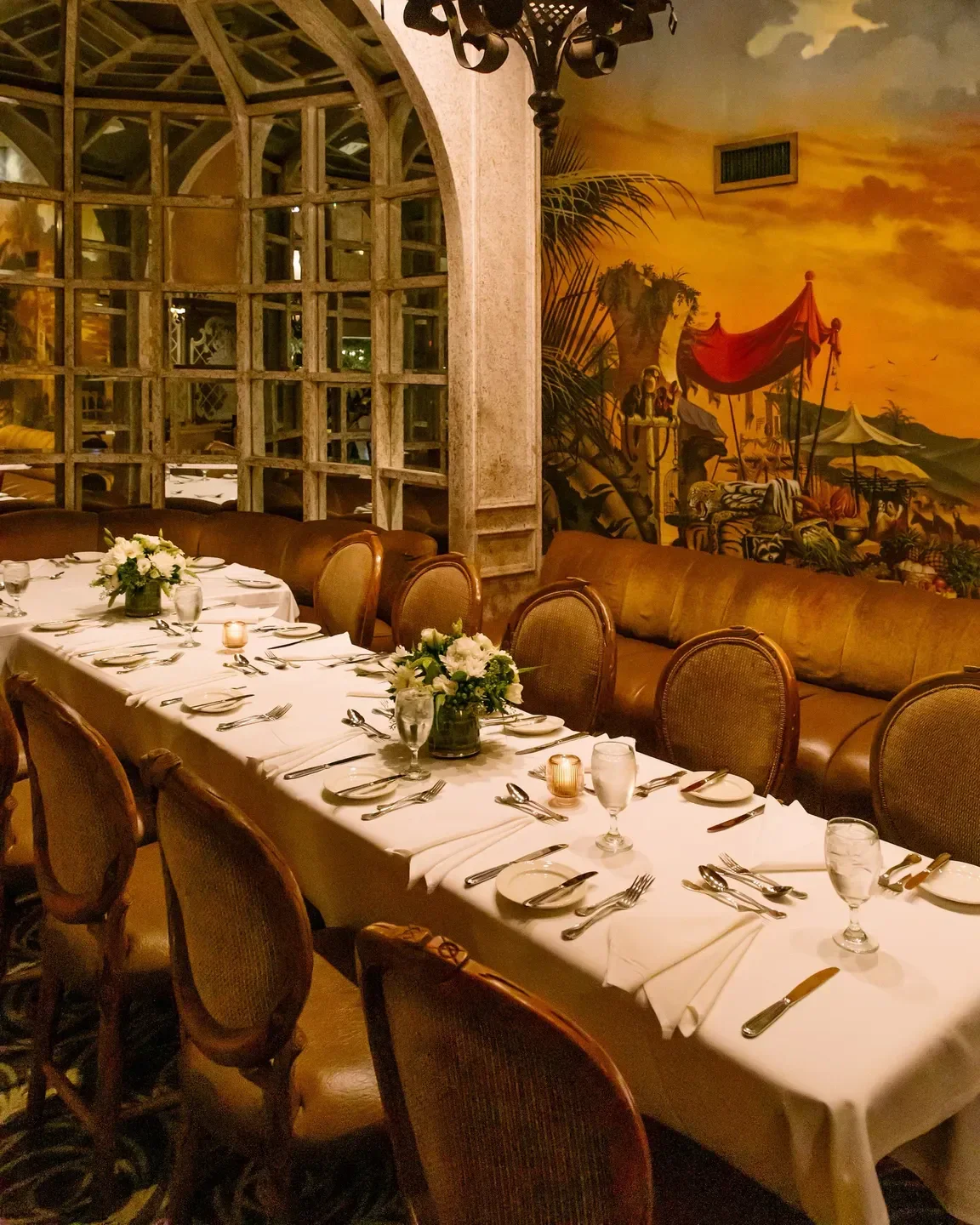Elegant dining room interior at Wally's Desert Turtle in Palm Springs, featuring a mural and tables.