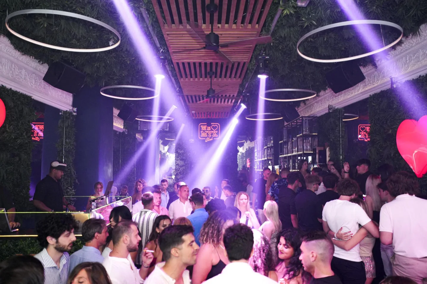 Vibrant interior of WE LOVE MYK nightclub in Mykonos with purple lights and lush greenery