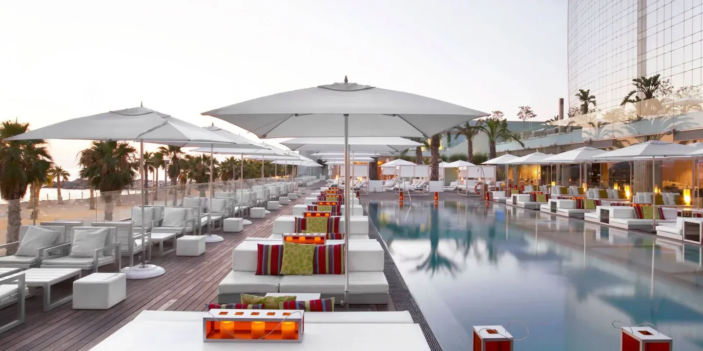 Chic lounge area at Wet Deck beach club in Barcelona, with a pool and parasols.