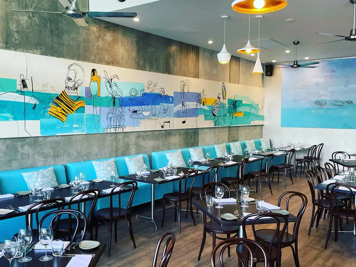 Stylish interior of Wrasse & Roe restaurant in Port Douglas, with art and turquoise seating