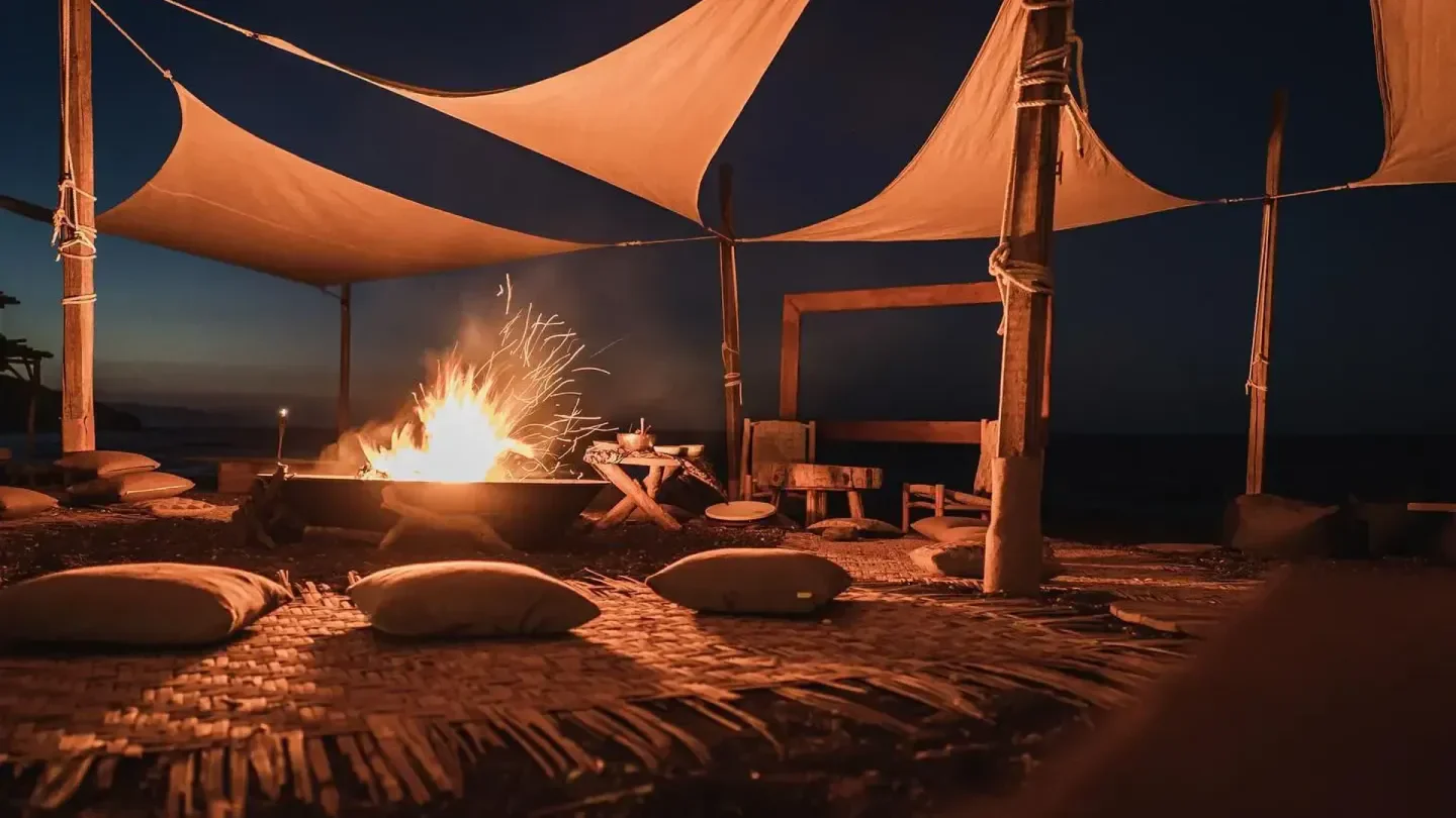 Cozy bonfire at Yalos Beach Club in Santorini, with cushions and a shaded area.