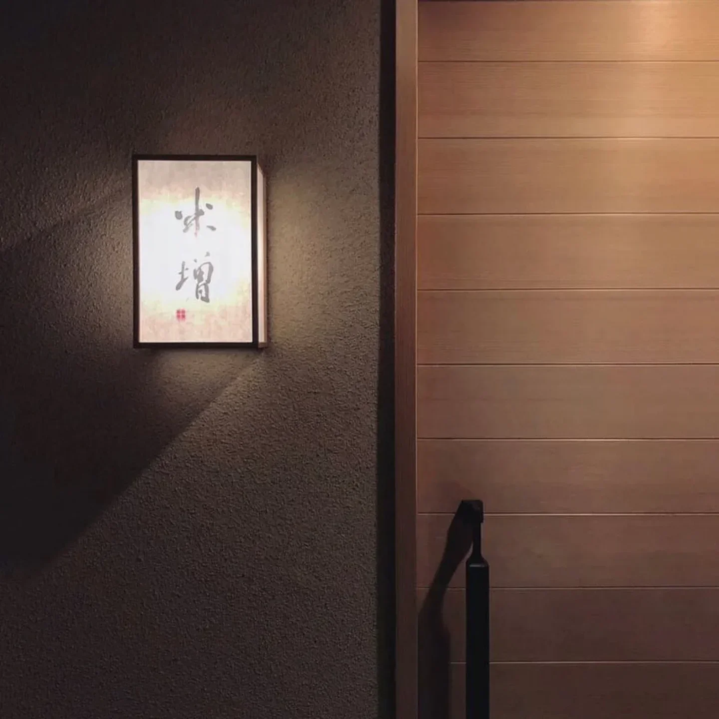 Entrance detail at Yonemasu restaurant in Osaka, featuring a glowing sign and wooden door.