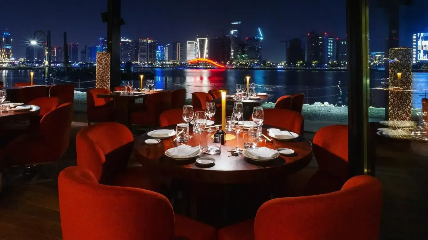 Zuma Doha: Night view of restaurant interior with city skyline and waterfront.