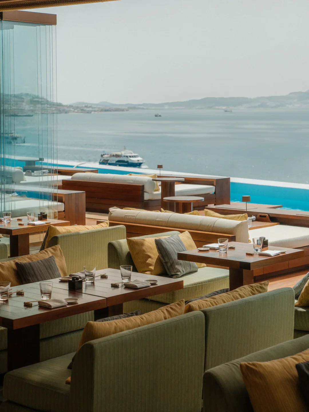 Outdoor seating with sea view at Zuma restaurant in Mykonos, featuring plush cushions and elegant tables.