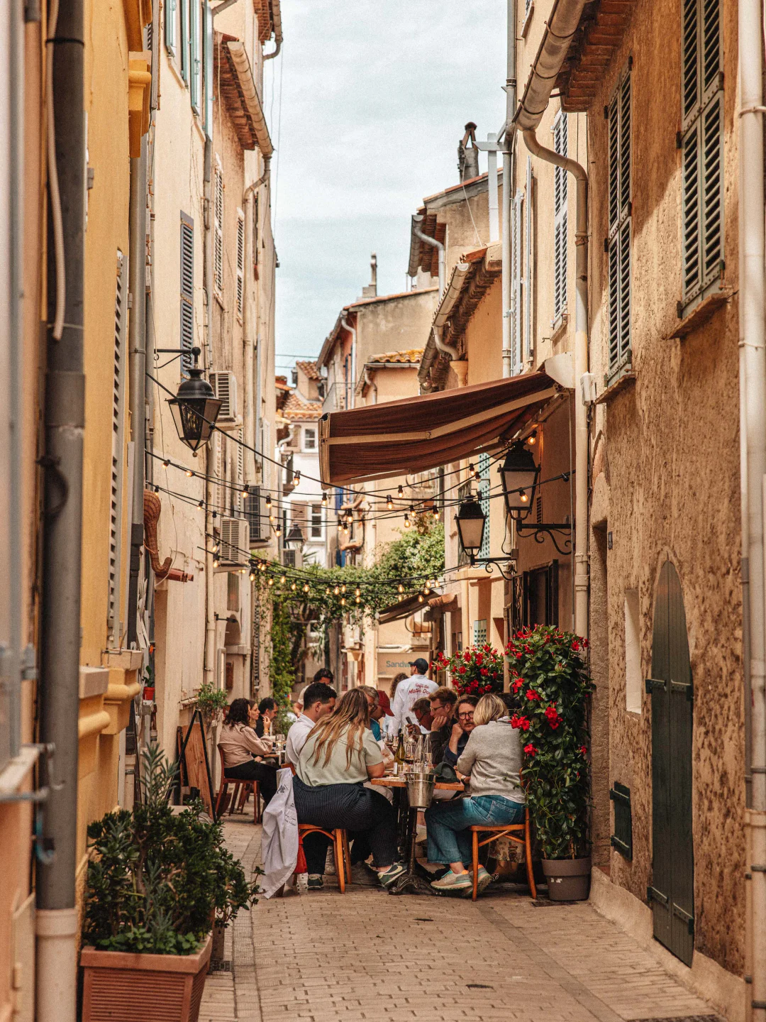 Charming alleyway dining at Zuma Saint-Tropez with people enjoying a meal amidst string lights and greenery.